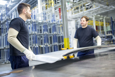 Two colleagues carrying bonnet in car factory