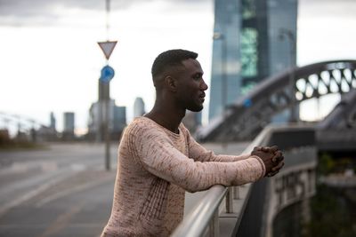 Young man looking away while standing on bridge