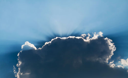 Low angle view of sunlight streaming through clouds