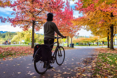 Rear view of man riding bicycle on autumn leaves