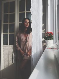 Young woman standing by window at home