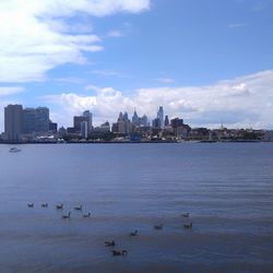 View of city at waterfront against cloudy sky