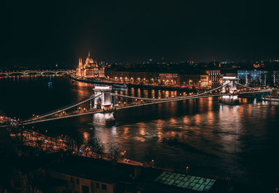 Illuminated bridge over river in city at night