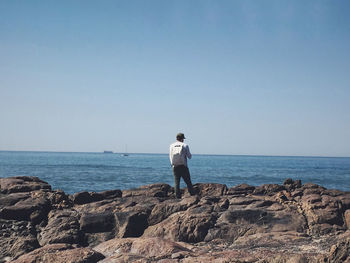 Man standing on rock looking at sea against clear sky