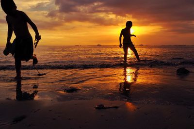 Silhouette people on beach against sky during sunset