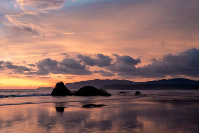 Silhouette rock in sea against sky during sunset
