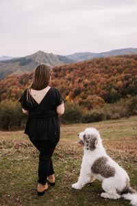 Back view of unrecognizable female walking along hill with spanish water dog and enjoying nature in highland area