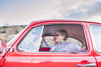 Cheerful senior couple traveling in red vintage car