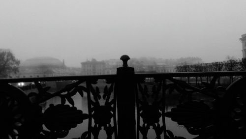 Railing by river in city during foggy weather