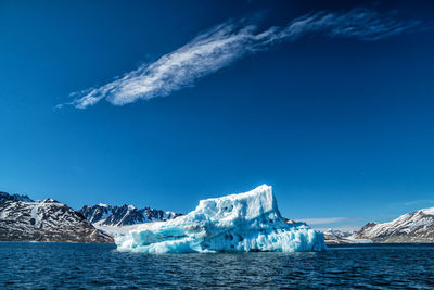 Scenic view of sea by snowcapped mountain against blue sky