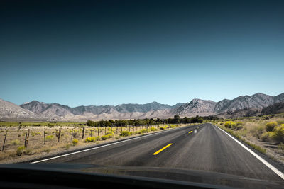 Road leading towards mountains against clear sky