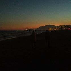 Silhouette man standing on beach against clear sky at sunset