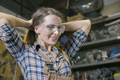 Close-up of smiling woman tying hair in workshop