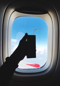 Silhouette hand holding drink against airplane window