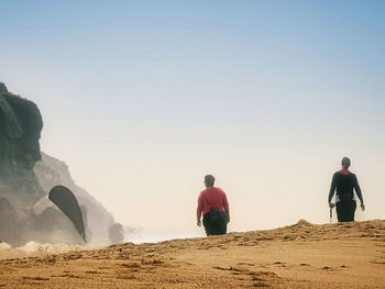 Rear view of men on rock against clear sky