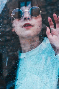 Portrait of woman wearing sunglasses seen though wet window