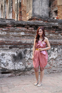 Portrait of smiling young woman standing against brick wall