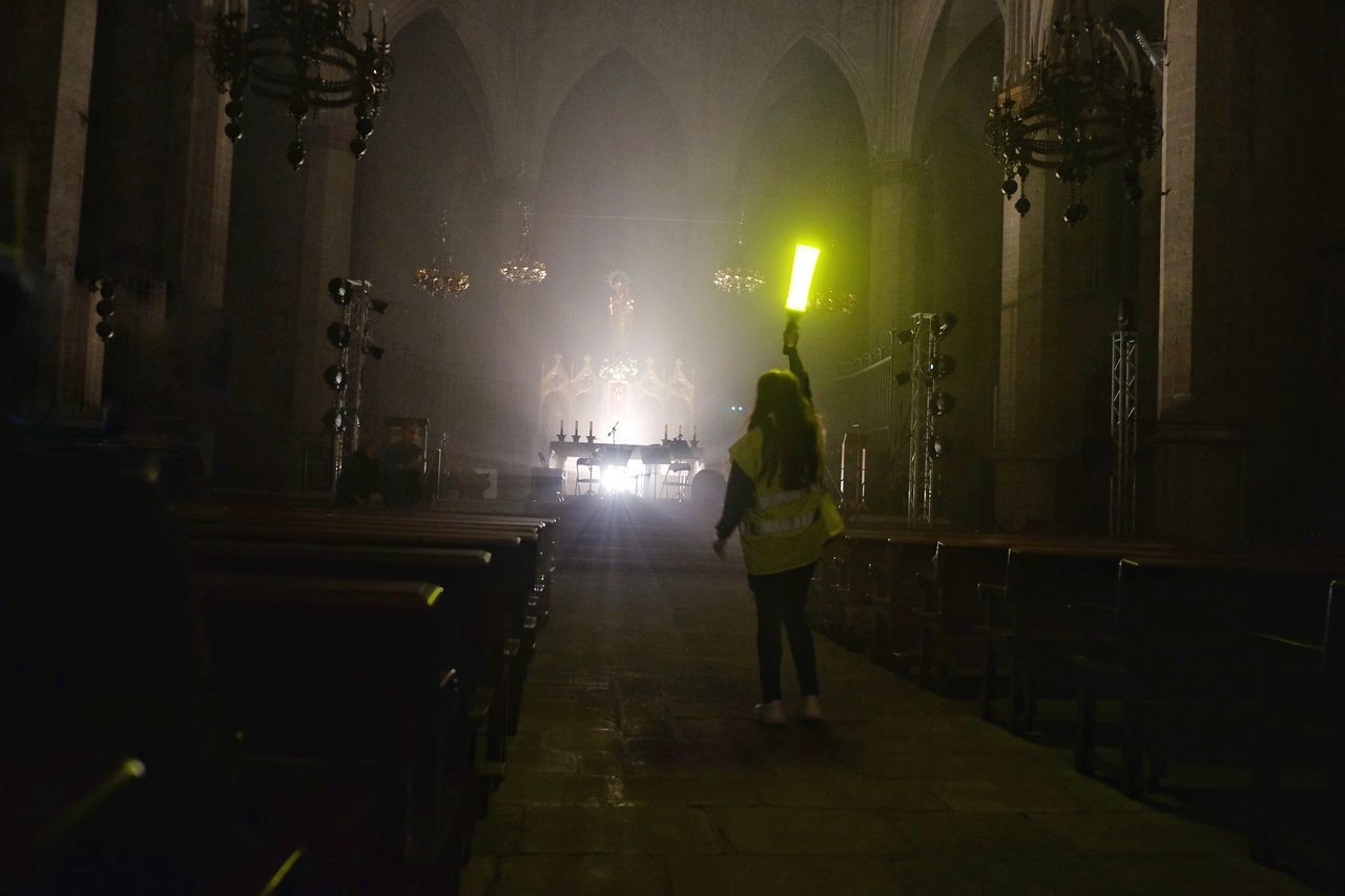 REAR VIEW OF MAN STANDING BY ILLUMINATED BUILDING