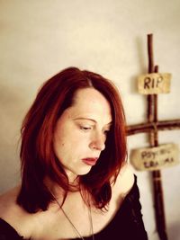 Sad woman standing with cross and text hanging on wall