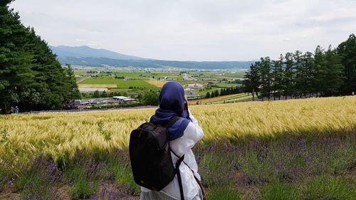 Rear view of woman with backpack standing on field against sky