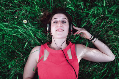 High angle portrait of young woman listening music while lying on grassy field