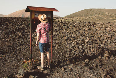 Rear view of man reading information sign while standing on field against sky