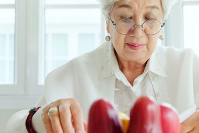 Fruits on table with senior woman reading book in background