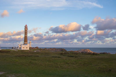 Lighthouse on field by sea against sky