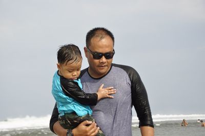 Father and son at beach against sky