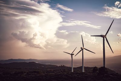 Wind turbines on land against sky during sunset