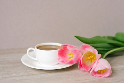 Coffee with milk in a white porcelain cup and saucer, a bouquet of spring pink tulips. mother's day