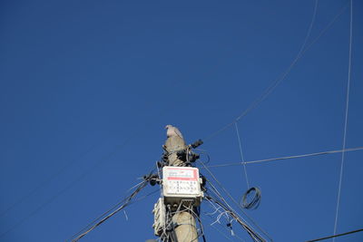 Low angle view of telephone pole against clear blue sky