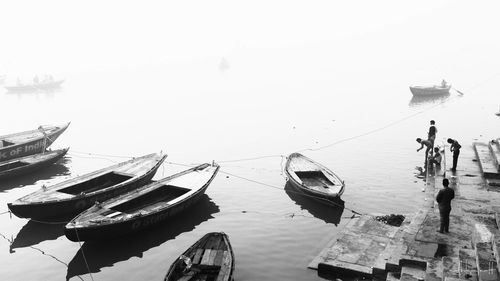 People on boats moored in sea against sky