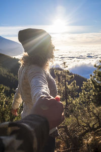 Cropped image of man holding woman hand against sky