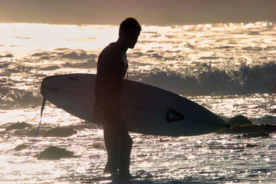 Silhouette man with surfboard on beach during sunset