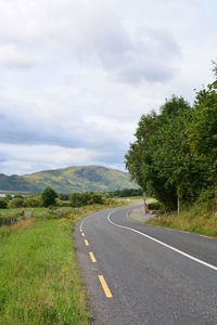 Empty road by trees against sky