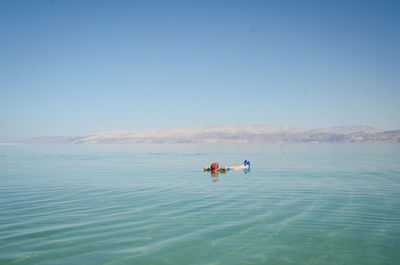 People in sea against clear blue sky