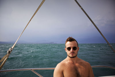 Portrait of shirtless man wearing sunglasses in boat on sea against sky