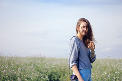 Portrait of young woman with blond hair standing on field against sky