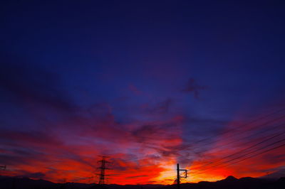 Low angle view of silhouette electricity pylon against dramatic sky