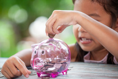Girl putting coin in piggy bank at table