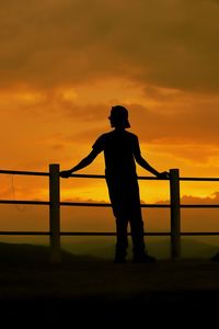 Silhouette man standing on railing against orange sky