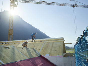 Coworkers installing wooden roof on sunny day