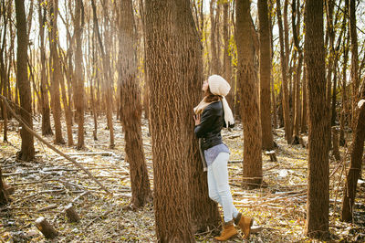 Side view of young woman while standing by tree in forest