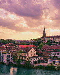 River amidst buildings in town against sky at sunset