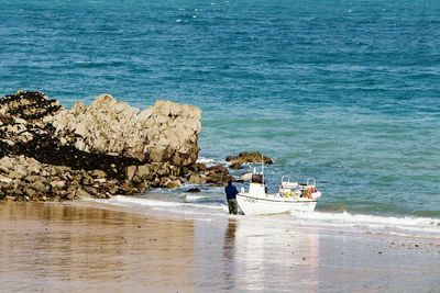 Rear view of man standing by boat moored at beach