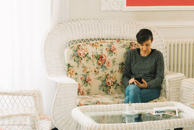 Woman using mobile phone while sitting on chair at home