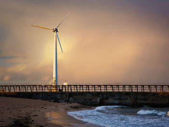 Windmills on sea against sky during sunset