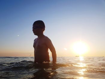 Boy looking at sea against sky during sunset