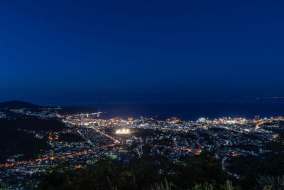 High angle view of illuminated city by sea against sky